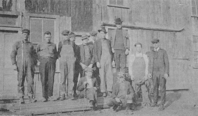 The Bill Jones blacksmith shop and hall in the early twenties. Tom Osborne (seated, with cane) ran the shoe shop, livery stable, and hotel. Others in the picture are Rudolph Downing, Carl Clements, Charlie Jones, Tude Nagels, Charlie Dillon, Orville Stout, Don Sullenger, Oscar Dillon, Lawrence Davis, Fullie Reynolds, John Teigue.
