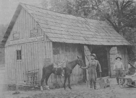 Blacksmith Shop at Swan, about 1906. Bill Jones at left, and J. G. Burger II and J. G. Burger III at wheelbarrow.