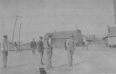 STREET SCENE about 1916. The first building on the right, of which a corner is visible, is the Baptist Church. The house in the center background was the home of Ben Jones who taught a subscription school for those students desiring more than the usual three months a year. It was the custom of the young men around town to challenge the school boys to games of Dare Base, and such a game was in progress when this picture was taken. After a snow fall, snowball fights replaced Dare Base as the order of the day.