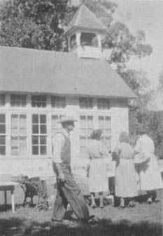 South side of Cedar Bluff school, taken at one of the reunions.  Leonard Wilson, brother of Rosa Steele in foreground.  Other persons in picture not known.